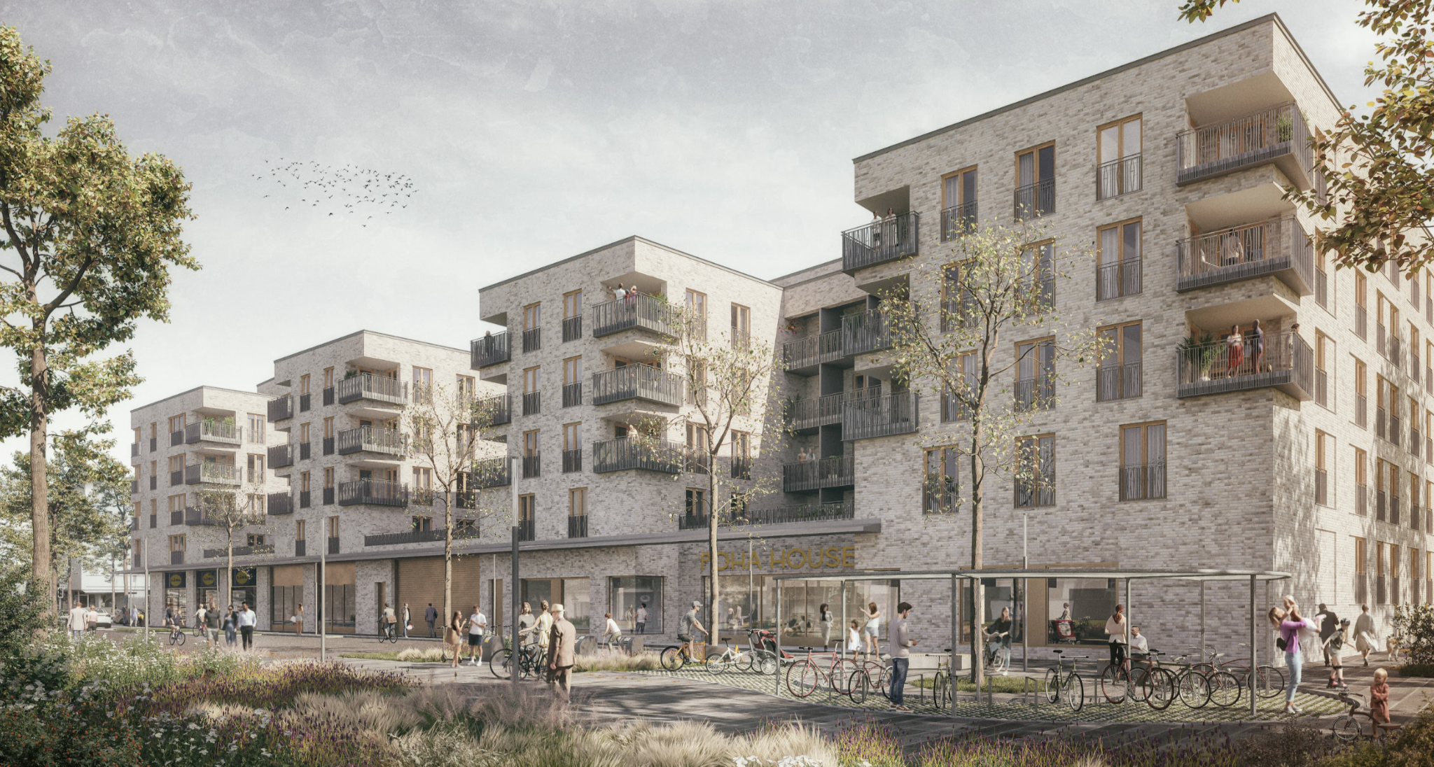 An architectural rendering of POHA House in Düsseldorf, featuring a modern, multi-story apartment complex with a light-colored brick facade and numerous dark-railed balconies. The ground floor consists of retail spaces with large glass windows, including a visible "POHA House" sign. The scene is a vibrant, pedestrian-friendly urban plaza filled with people walking, cycling, and congregating near bike racks under a clear, soft sky. Long grasses and trees frame the foreground and side, giving the development a sustainable, community-oriented atmosphere.