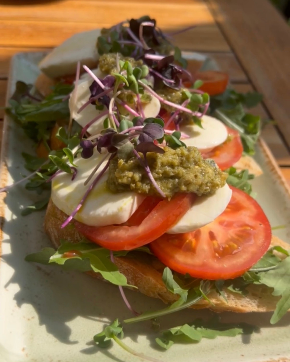 Open-faced caprese sandwich with fresh mozzarella, sliced tomatoes, pesto, microgreens, and arugula.