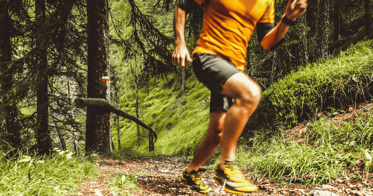 A person trail running on a dirt path through a forest